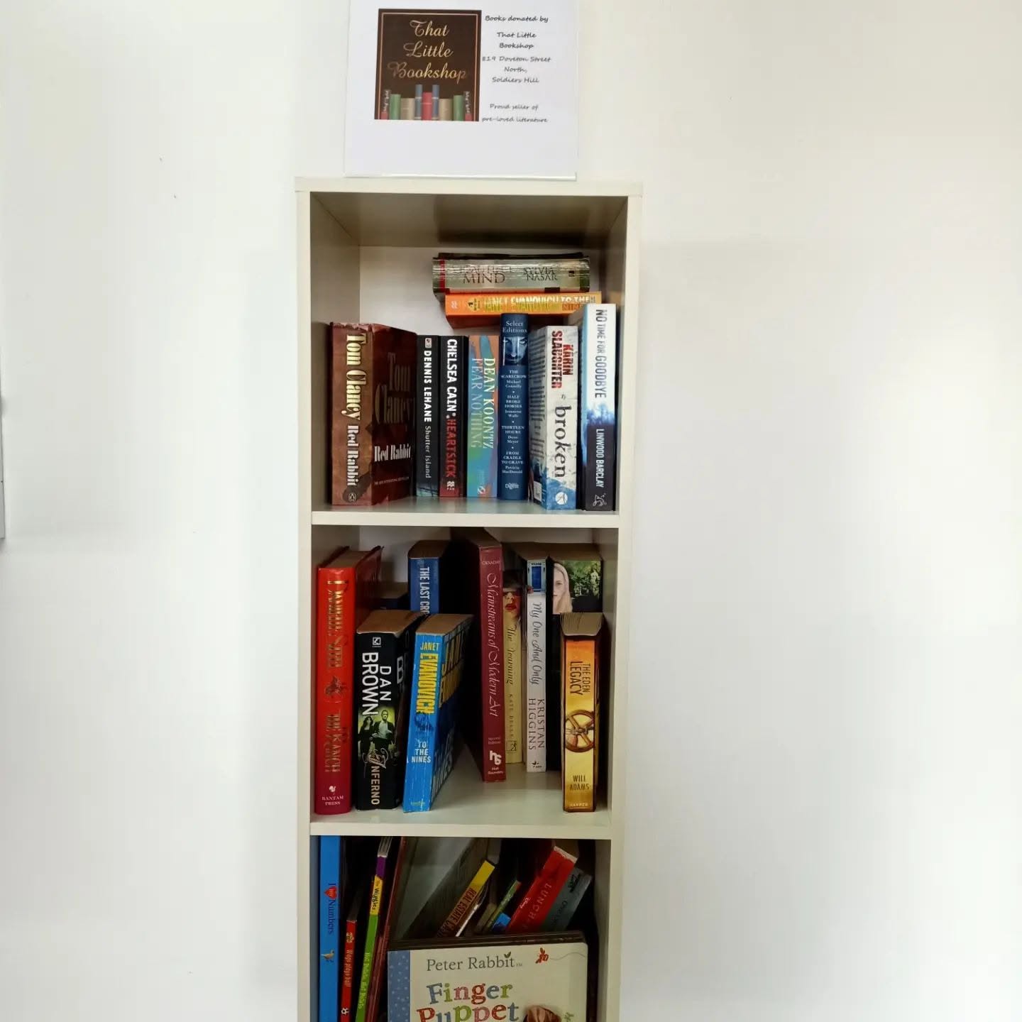 Bookshelf of donated books with a That Little Bookshop sign