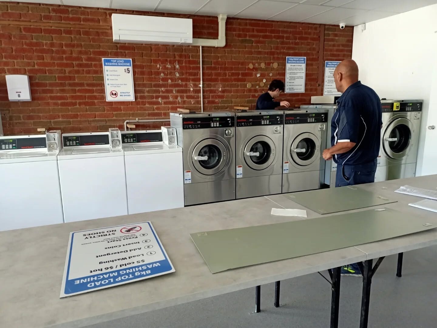 Top-load and stainless front-load washing machines in front of a brick wall